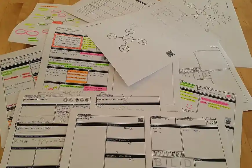 Printed weekly planning sheets on a table, rows marked up in highlighter
