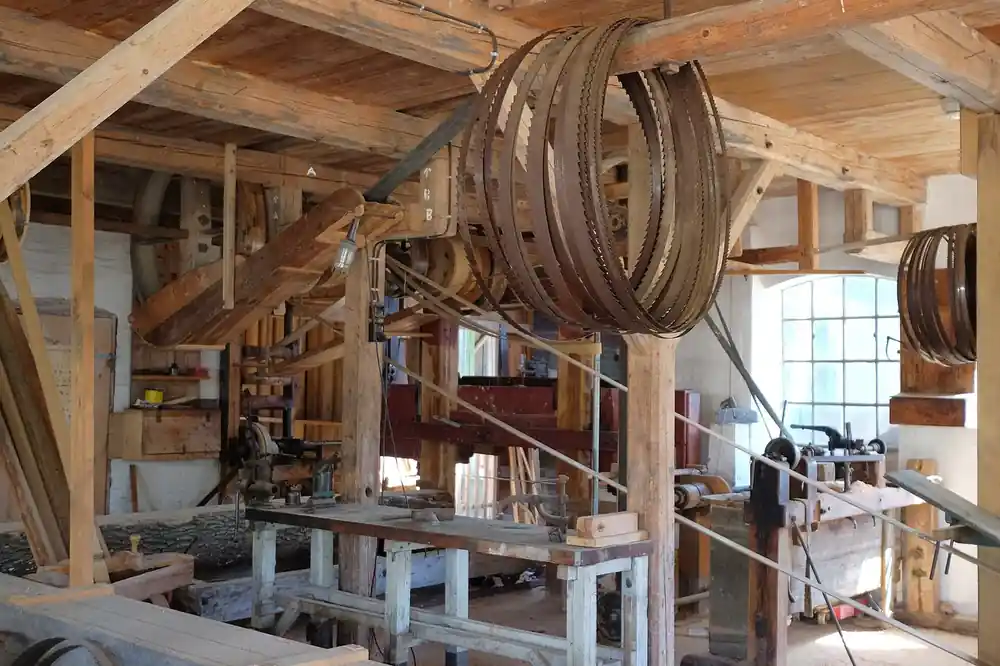 A timber-framed workshop with benches, saw blades hanging from a beam