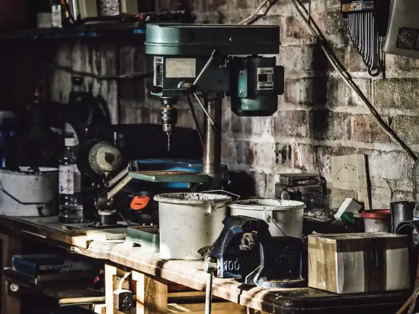 A workshop bench with a pillar drill and tins of parts